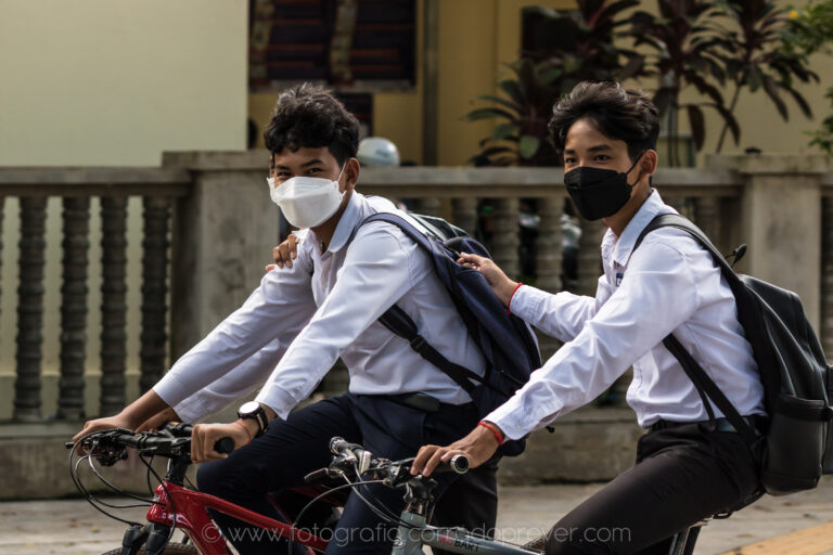 Altri due studenti in bicicletta, zaino in spalla e mascherina.