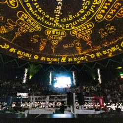 Il ring sotto la cupola decorata del Rajadamnern Stadium, con il pubblico che prende posto per la serata di muay thai.